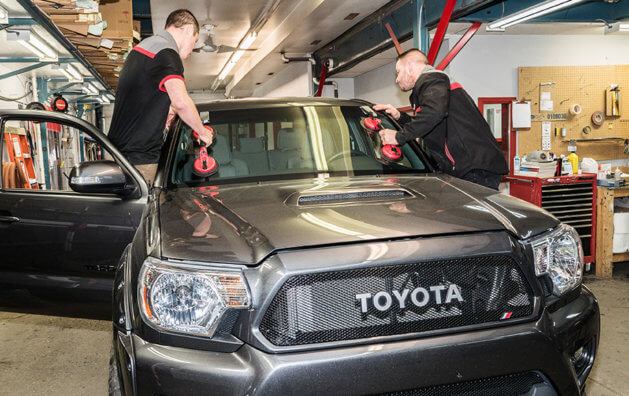 two mechanics repairing the front glass of a toyota truck