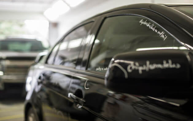 Photo of the side of a black car with a text written with white down on the edge of the passenger window and one of the side mirrors.