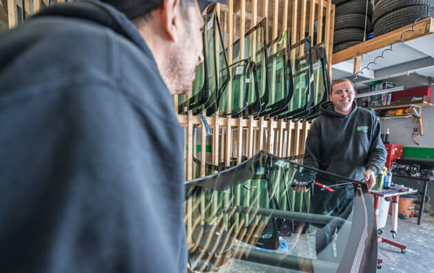 Two men holding a windshield with windshield replacement set about to place it in a car.