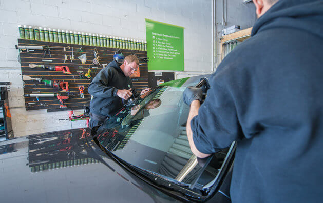 Two men loading a windshield with windshield replacement set by placing it in a car.