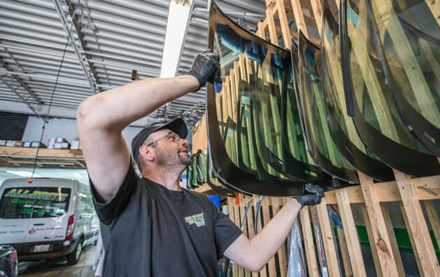 A man catching a new windshield from the wooden shelves.