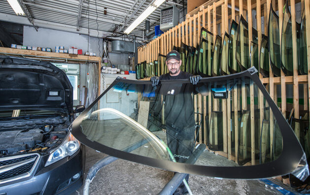 A man holding a new windshield before placing it in the car.