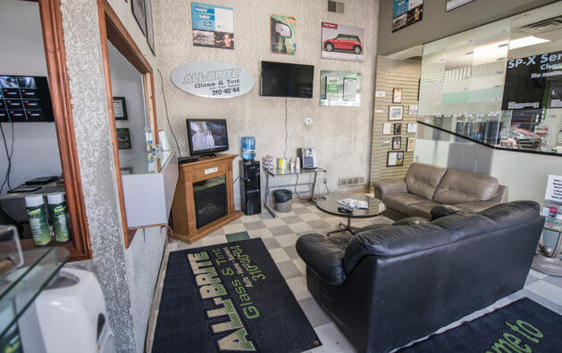 Waiting area with two large leather armchairs placed perpedicularly, and a small round glass table in the middle photographed from the entrance door.