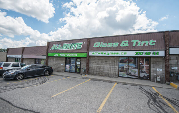 The front of All-Brite Glass & Tint with two glass doors. The name of the company is written in green and large capital letters above seen from the right.