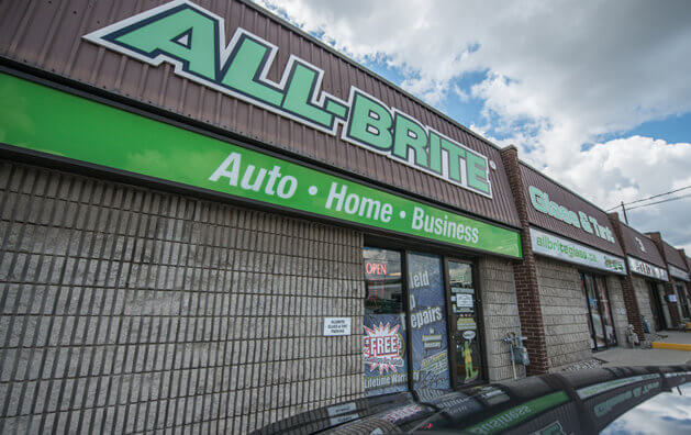 The front of All-Brite Glass & Tint with two glass doors. The name of the company is written in green and large capital letters above.